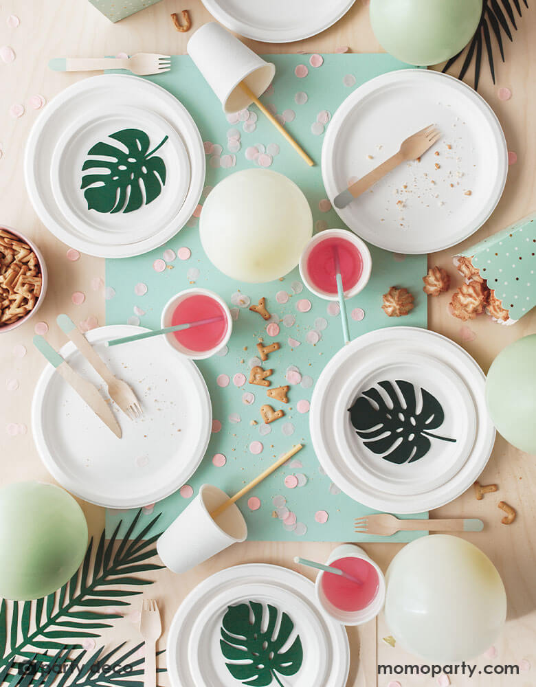 A overhead shot of a tropical themed party table featuring some solid colored tableware adorned with Momopartys's tropical leaves paper decorations in different designs and shades of green. A perfect info for a summer tropical or fiesta themed celebration.