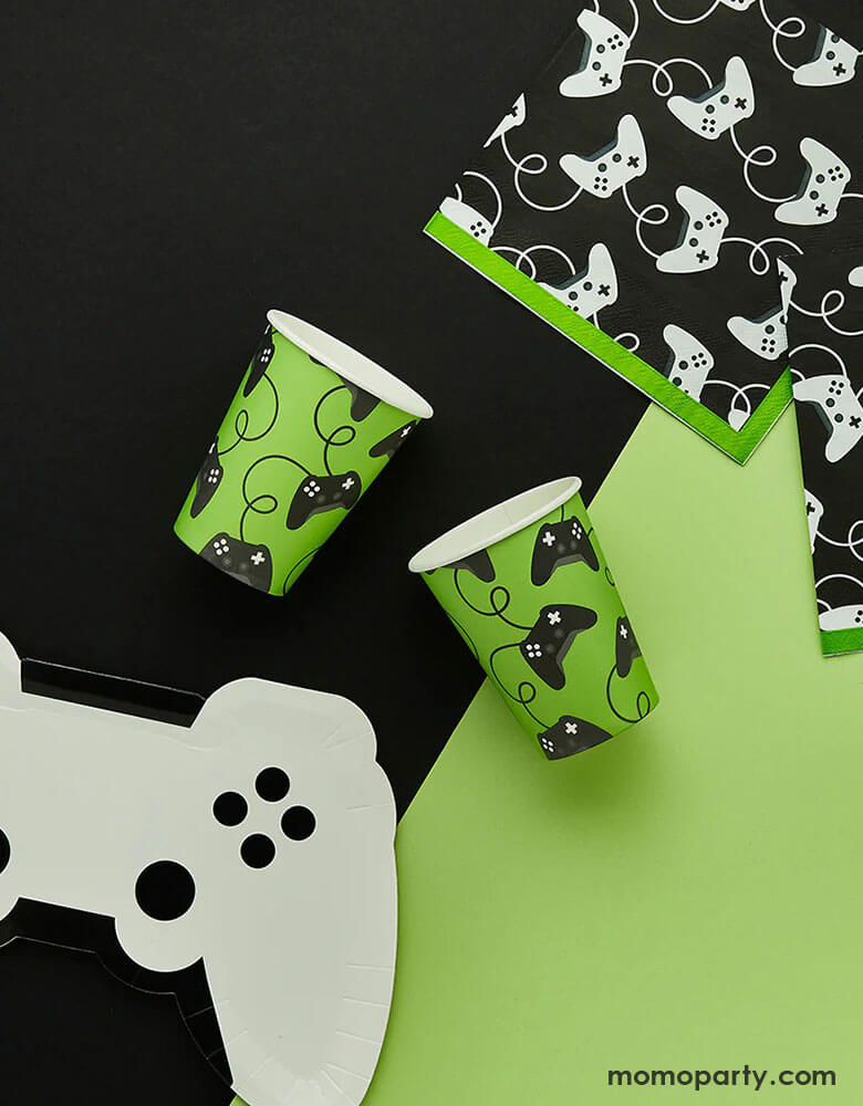 A video game themed party collection from Momopartys by Hooty Balloo including a white video game controller shaped paper plate, two green video game controller motif party cups, and two black game controller motif large napkins with green edge, all on a classic black and green color blocked background, perfect for any game events or a kid's video game themed birthday party.