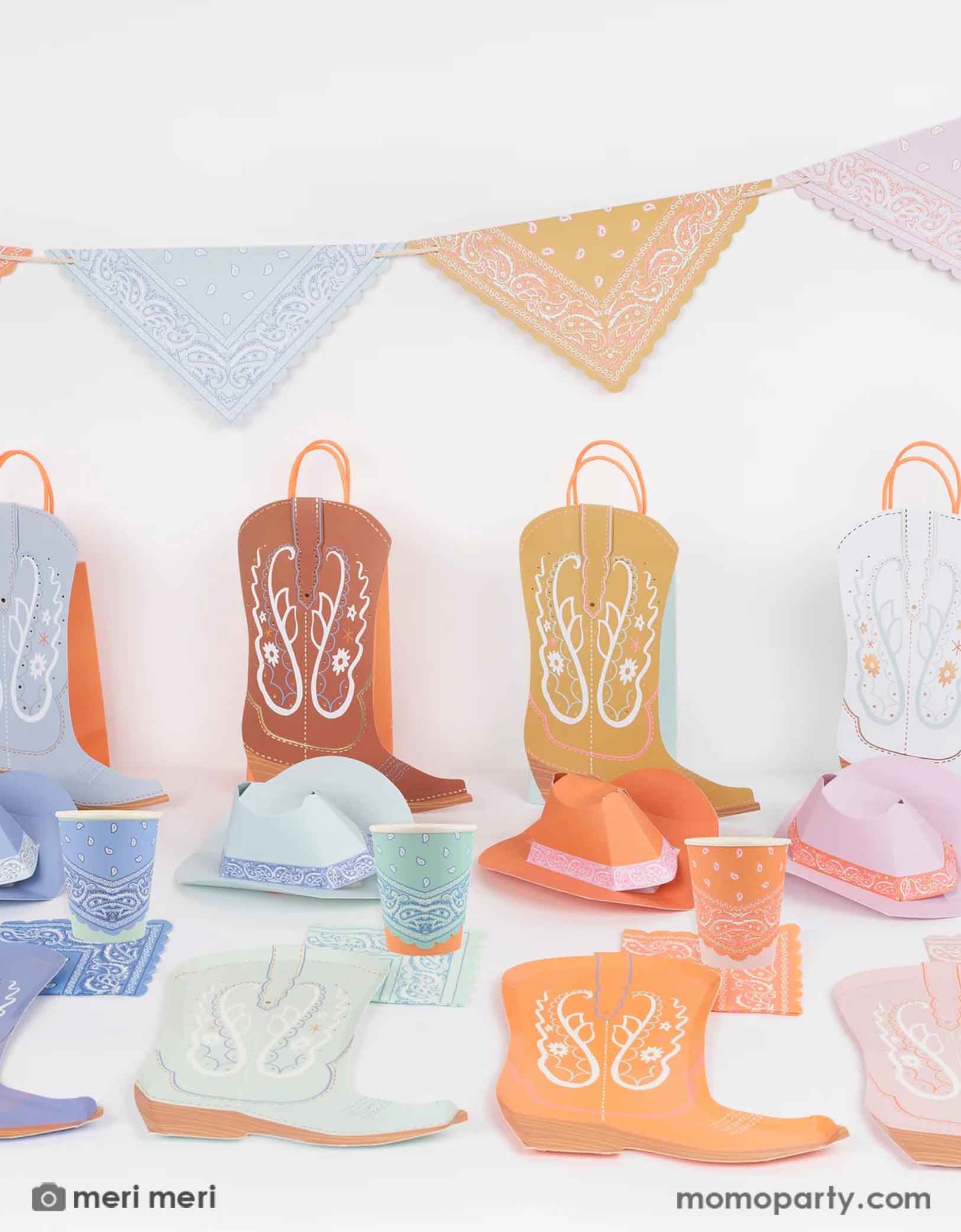 A Western themed party table featuring various cowboy inspired party good by Meri Meri from Momopartys, including boot shaped plates, bandana party cups. boot shaped party bags and bandana flag party garland in multiple pastel colors. Perfect for a Western themed party or kid's "First Rodeo" first birthday party.