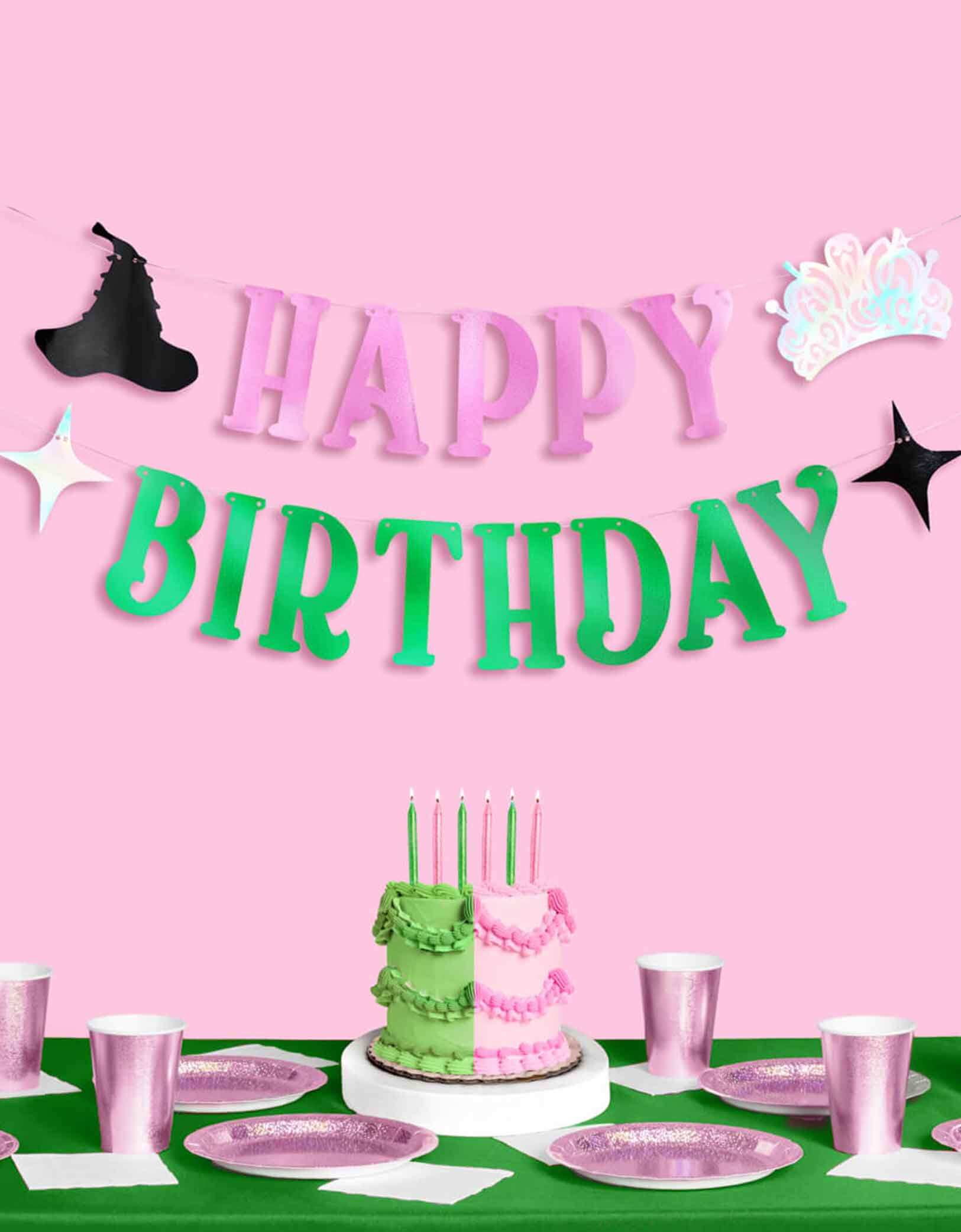 A Wicked themed Birthday party setup with pink and green decorations from Momopartys, including a cake with glittered green and pink birthday candles,  the Wicked 'Happy Birthday' banner, green tablecloth and glittered tablewares.