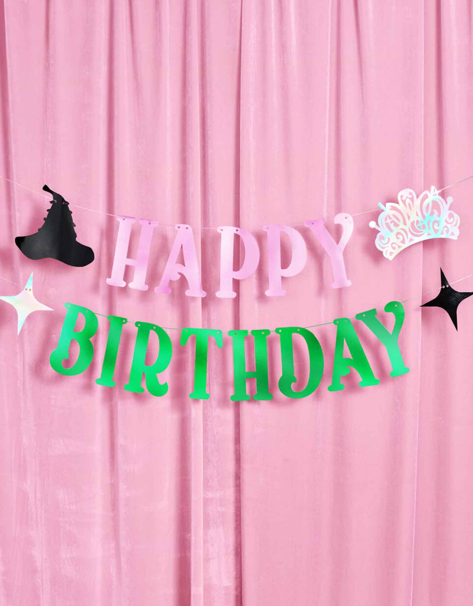 Momo Party's 4ft Wicked pink and green Happy Birthday banner with decorative elements including an iridescent tiara, a witch hat and star point pennants on a pink curtain background. 