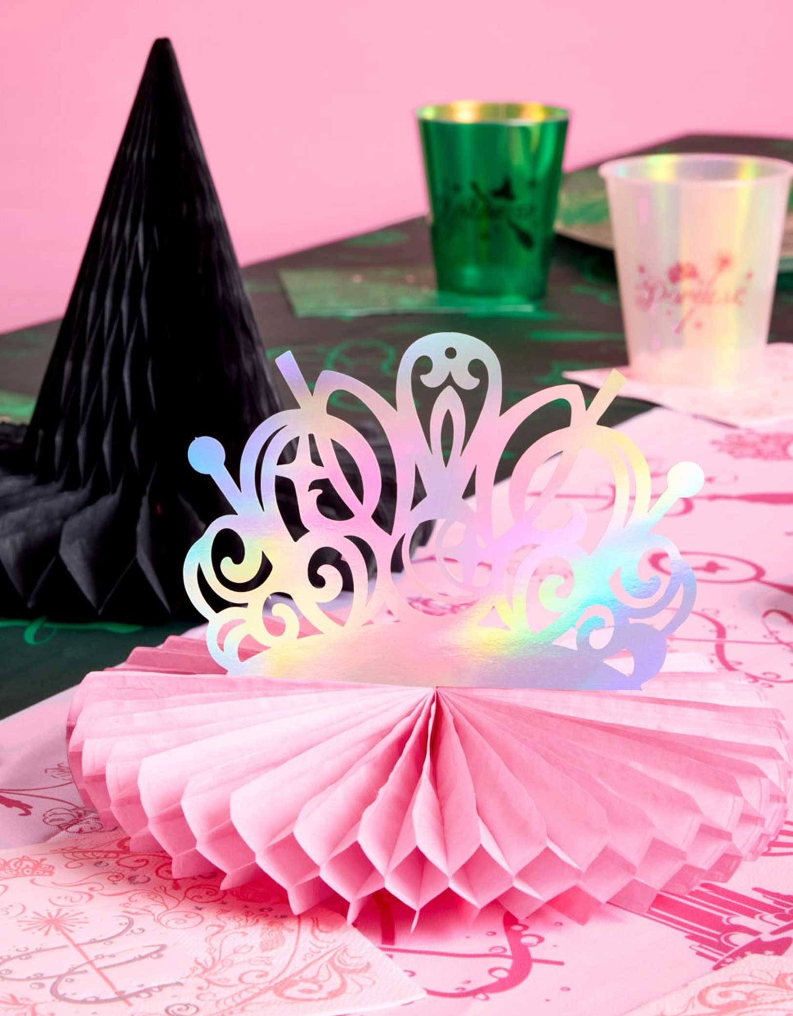 A festive Wicked themed party table featuring various of Wicked themed tablewares and decorations from Momopartys including Wicked Tiara & Witch Hat Honeycomb Set, Wicked party cups in green and green and Wicked party plates, napkins in green and pink on a Wicked themed tablecloth.