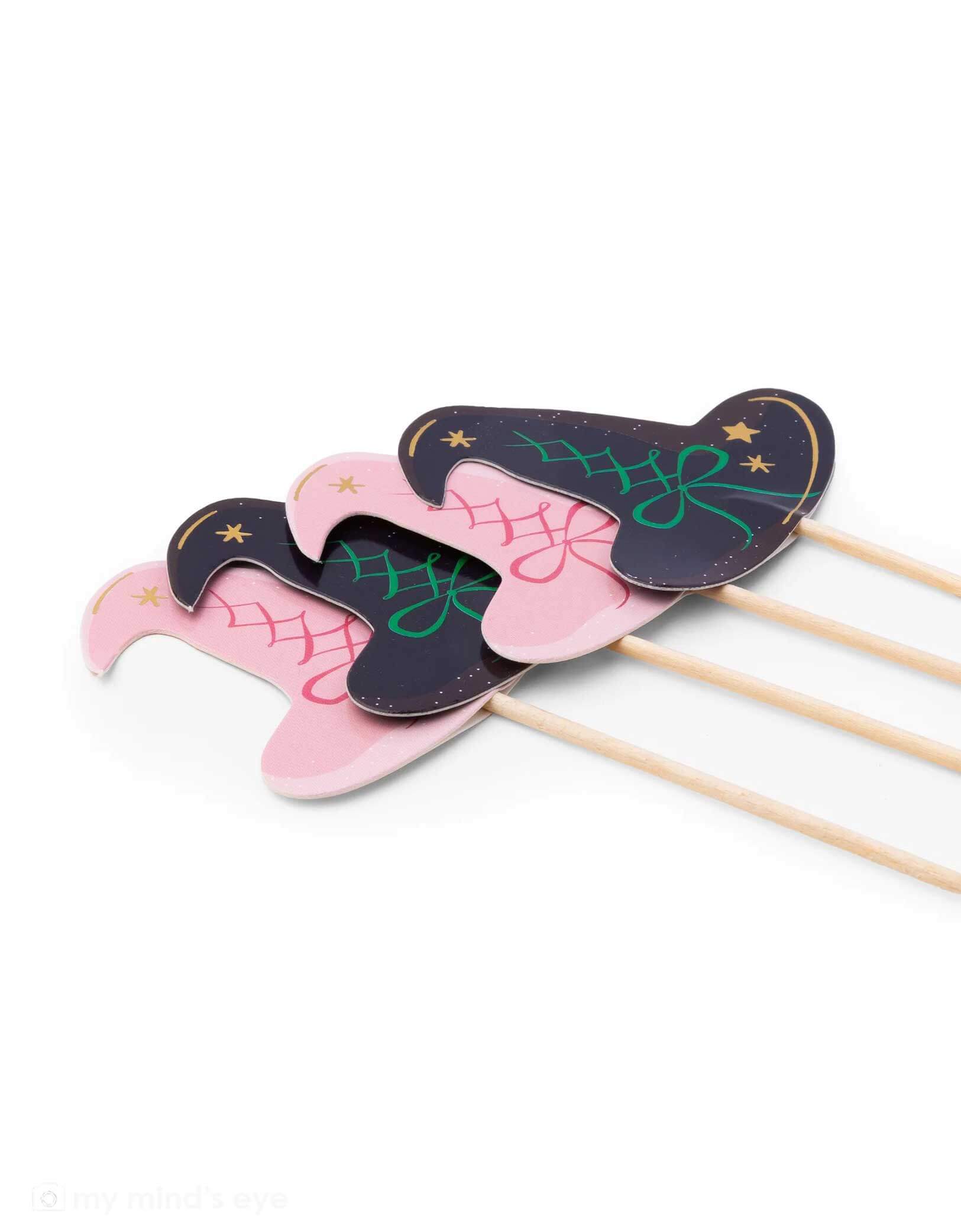Four witch hat cupcake toppers on sticks, two pink and two black with green accents from Momopartys, on a white background. These toppers are perfect for a Wicked themed party.