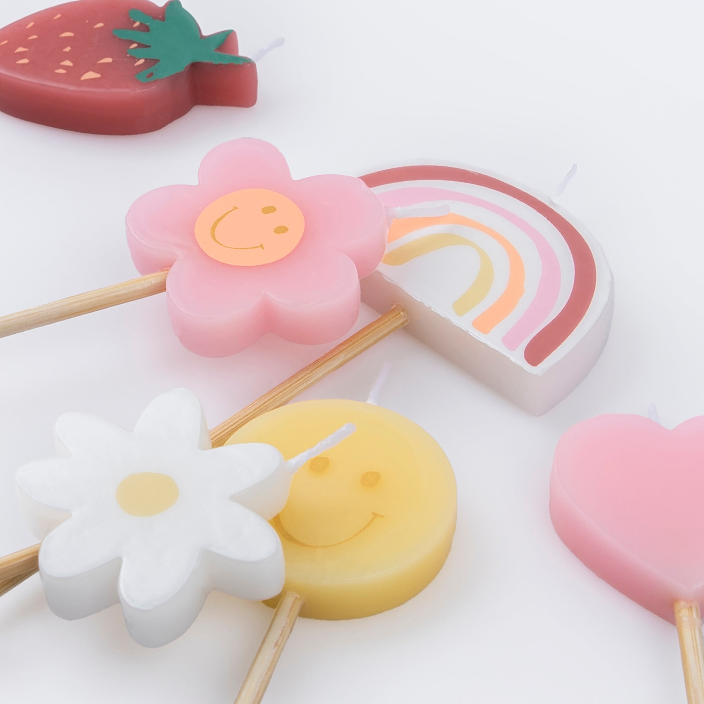 Details of Momopartys's Happy Face Icons Candles by Meri Meri. Featuring a set of 6 strawberry, a flower, a daisy flower, a rainbow, a smiley face, and a heart candle with long sticks, these colorful candles are perfect for any happy celebration!