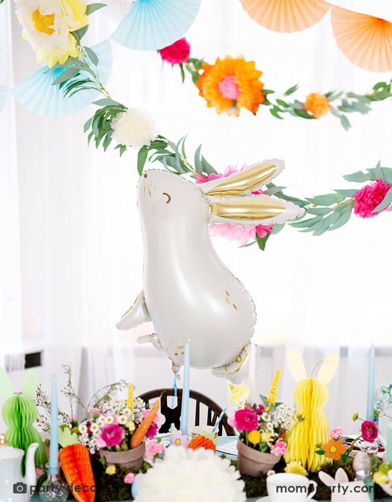 A beautiful Easter table decorated with spring flowers and honeycomb Easter egg, bunny and carrot decorations by Party Deco, with Momopartys's adorable 33 x 32" bunny shaped foil balloon by Party Deco in front of floral garland sets and tissue paper bunting garland, it makes a perfect inspiration for Easter celebration ideas.