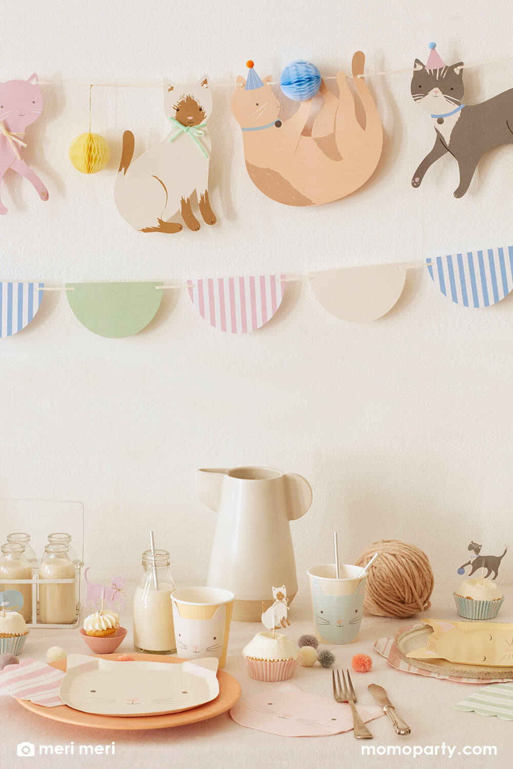 Momopartys kitten or cat themed birthday party, there is a Cute Kittens Garland set by Meri Meri on the wall. There are Cute Kitten Plates layered with coral plates, Cute Kitten Cups with silver straws, mike bottle, cupcakes with Cute Kittens Cupcake toppers, Ball of yarn, small pom poms on the table. These modern and cute design party supplies from Meri Meri of cat and Dog collection, are perfect decoration for a kitten or cat themed birthday party for kids or adults.