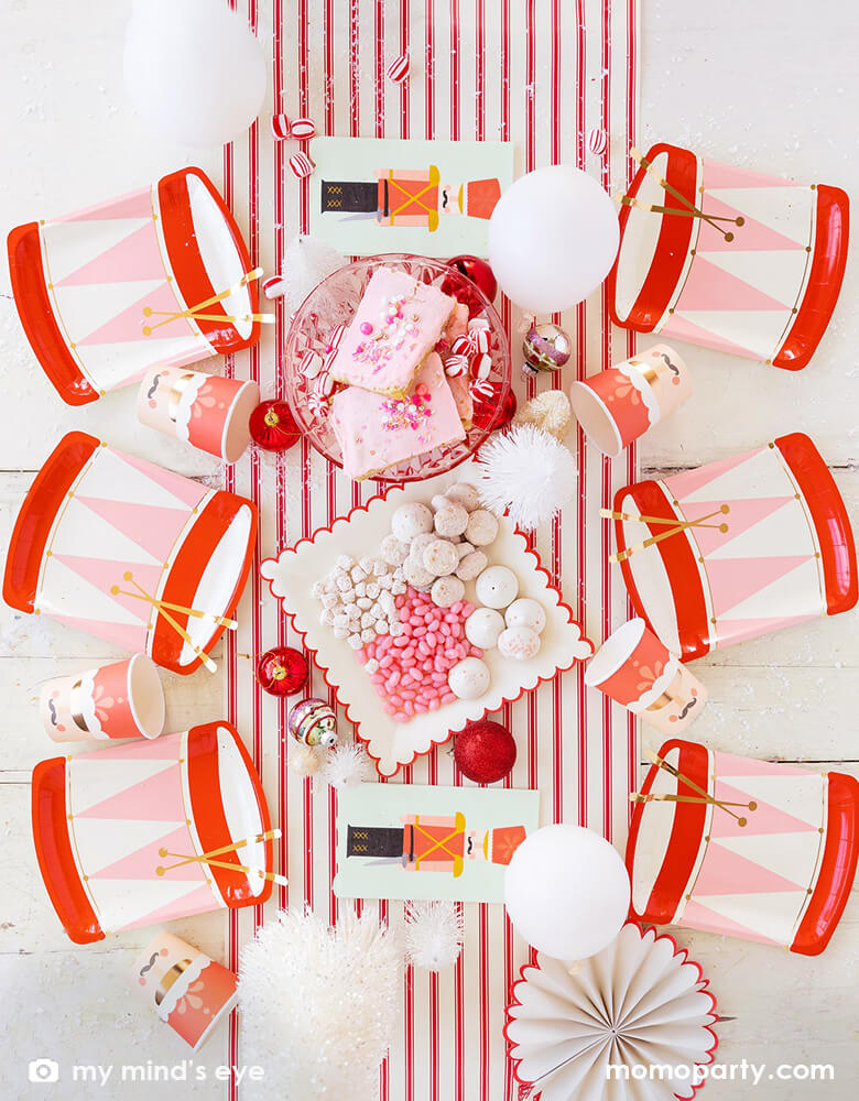 Holiday Christmas Family Table top view with Six My Mind's Eye Nutcracker Drum Shaped Plates, Nutcracker Napkins and Nutcracker Soldier Cups, sweets, cookies, ornaments, balloons and paper fan as center piece in the middle of the table over the Believe Christmas Red Striped Table Runner. These Morden and high quality party supplies with cute design in pink and red tone are so unique and adorable for holiday family gathering with kids and friends. Holiday partyware, party supplies at momopartys.shop