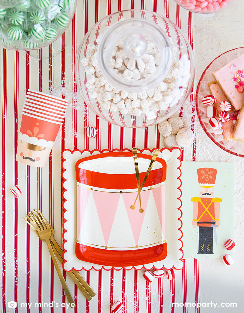 Holiday Christmas Table set up with My Mind's Eye Nutcracker Drum Shaped Plates layered with Believe White & Red Scalloped Large Plates, with Nutcracker Napkins and Nutcracker Soldier Cups, candy canes, a jar with sweets, cookies, and golden folks over the Believe Christmas Red Striped Table Runner. These Morden and high quality party supplies with cute design in pink and red tone are perfect for holiday family celebration with kids. Shop Holiday partyware, party supplies at momopartys.shop