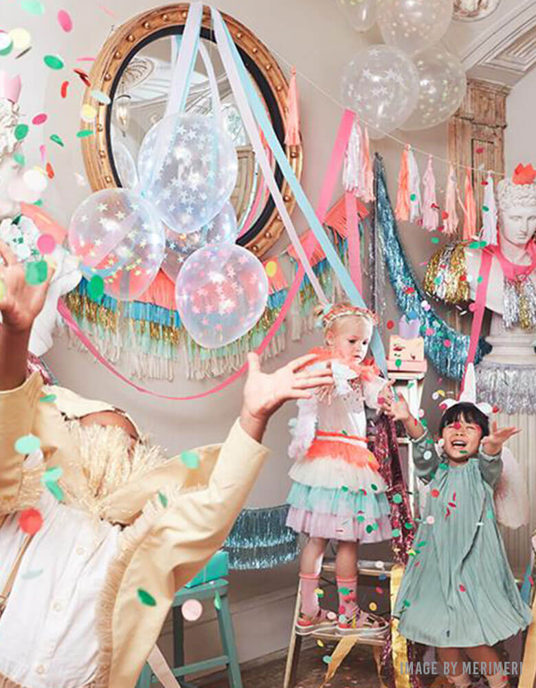 Kids Birthday party with Meri Meri's Colorful Fringe Large Garland decorated as the backdrop and kids throwing confetti 