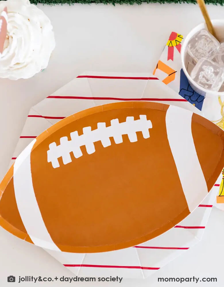 A close up of a sports themed party table featuring Momopartys's 7.5" good sport football shaped plates by Daydream Society. Come in a set of 8 plates, you can use these plates for team parties, birthday parties, and the Super Bowl! Go team!