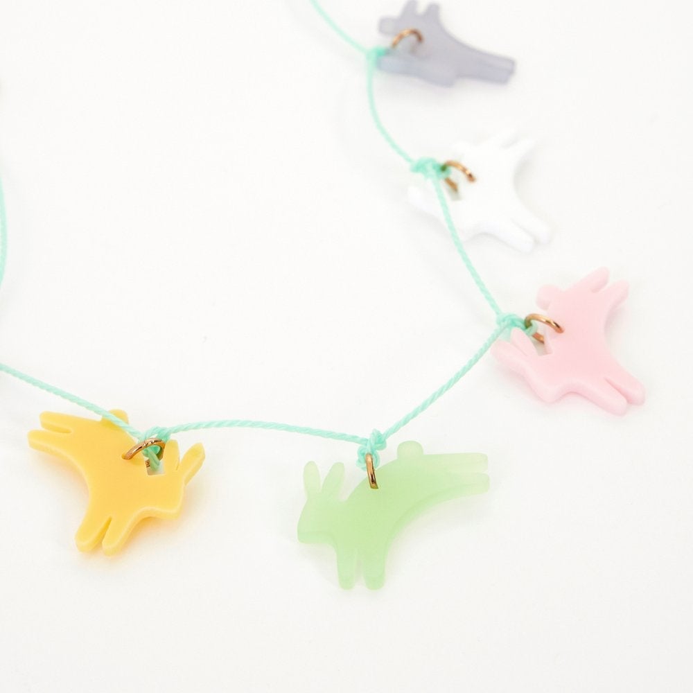 A close up of Meri meri Leaping Bunny Necklace. This bunny necklace is a wonderful accessory to wear to Easter, or springtime, parties. The bunnies are crafted from acrylic in 6 colors - frosted blue, white, frosted pink, frosted mint, yellow and pink, with a gold tone chain and mint cord necklace. A gold tone metal chain and lobster clasp give a stylish look.