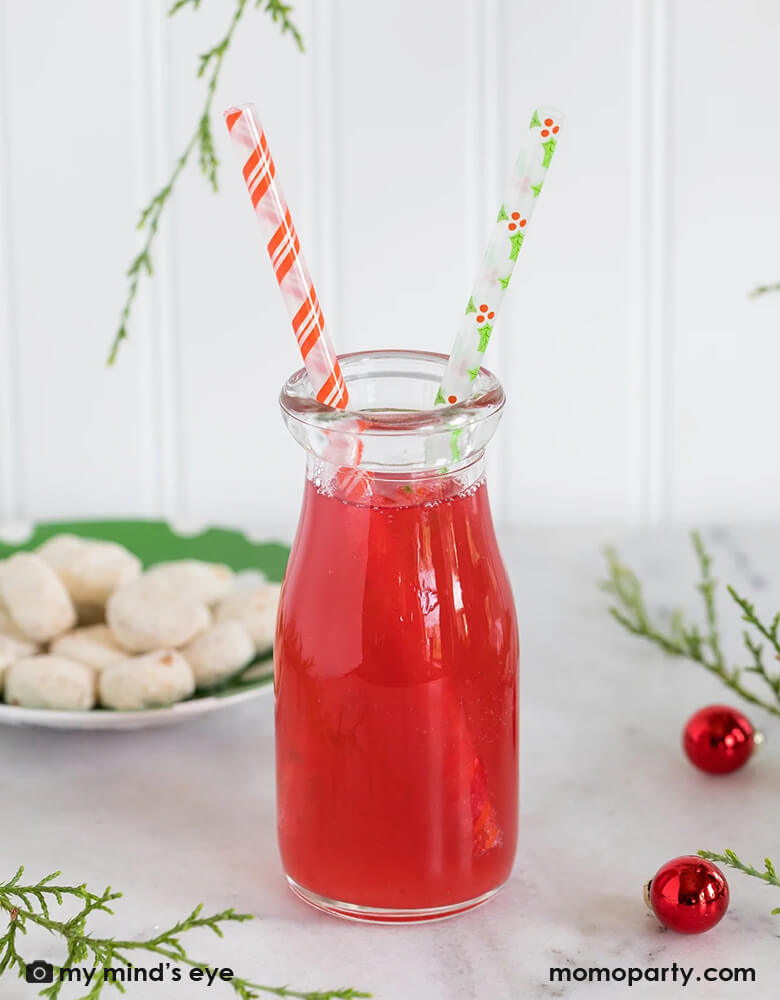 A holiday table with a cranberry juice bottle with Momopartys's Holly Reusable Straws by My Mind's Eye featuring festive Holly designs and Candy cane red stripes on the straws, perfect for this holiday season!