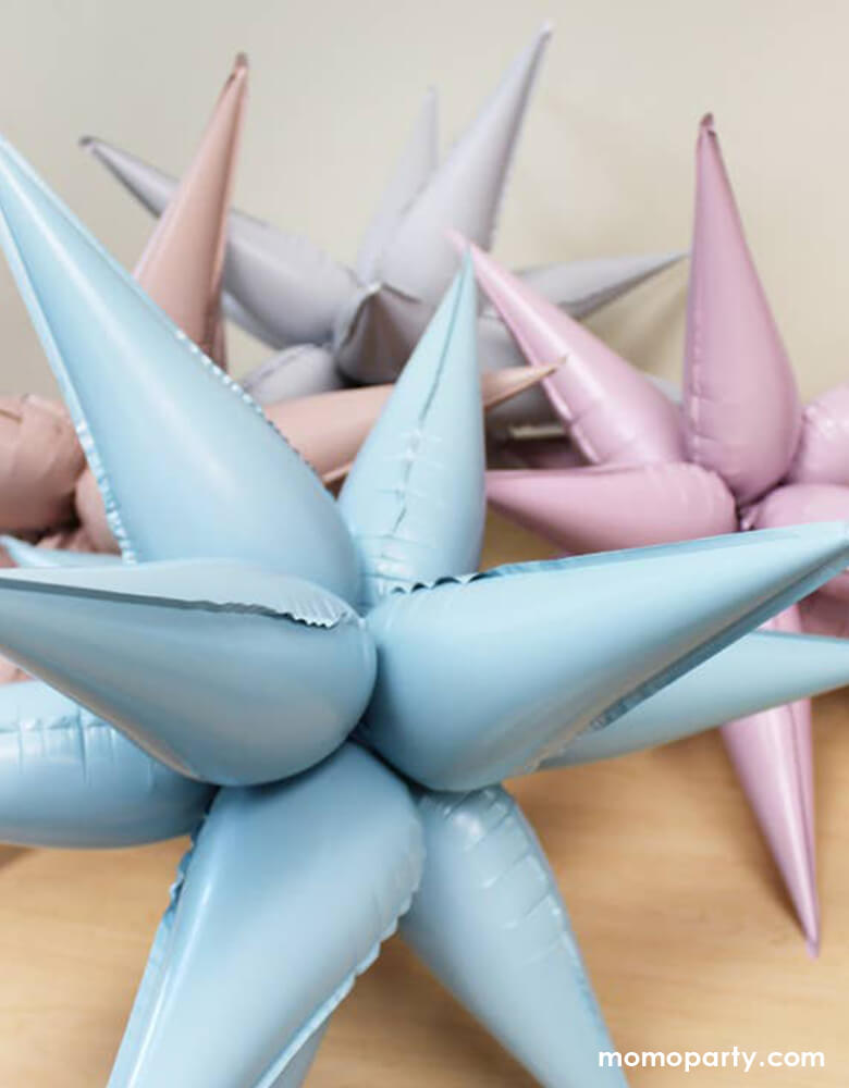 Set of 4 Momopartys's Jumbo 12 Point Starburst Foil Balloons in Blush, White, Pastel Pink and Pastel Blue colors display on the table. These 26 inches jumbo starburst foil balloons by Ellie's Party are simply a show-stopper for any celebration
