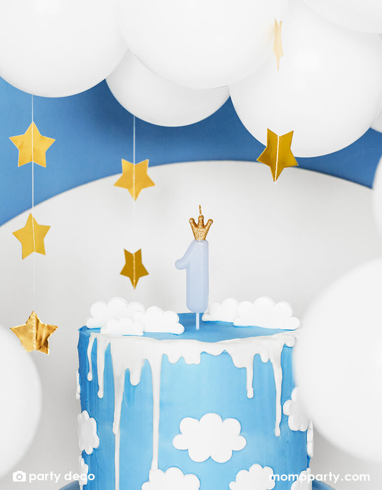 A blue birthday cake with cloud design on it which is topped with Momopartys's 3.5" blue Little Crown Birthday Candle by Party Deco, with star hanging garland in the back ground a beautiful white balloon cloud, it makes a prefect idea for a baby boy's first birthday party.