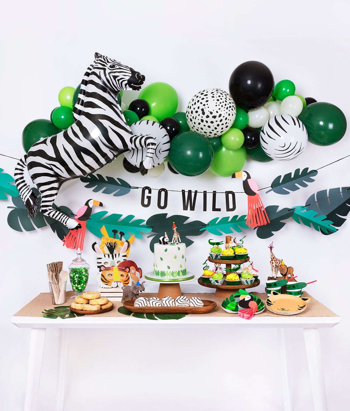 Momopartys jungle themed birthday party box with animal print balloon garland, zebra foil balloon, go wild garland decoration and tiger plates, tucan napkins, green foil plates, cake, cupcake, animal mask for kid's safari themed inspiration 