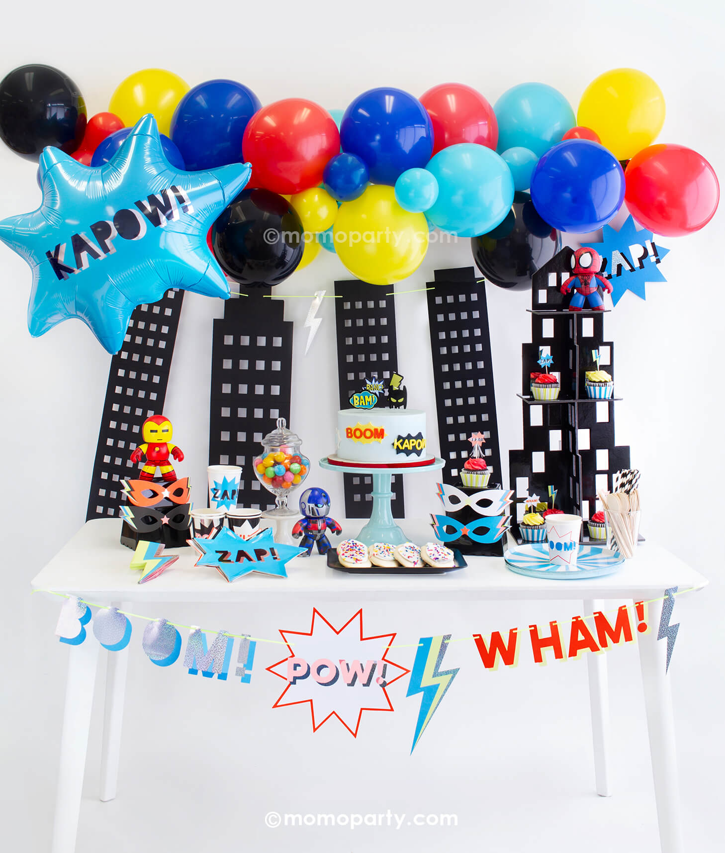 Momopartys Superhero Party Look. Decorated with Meri Meri Blue Stripe Dinner Plates, Superhero Plates, Party Cups, Lightning Bolt Napkins, Wooden Cutlery Set, Black Striped Straws, Cupcakes with toppers from Superhero Cupcake Kit, Superhero Masks, gumballs in a jar. Superhero Garland, Superhero Foil Balloon and colorful Superhero themed Balloon Cloud as backdrop. These modern party supplies are perfect for a boy and girl superhero themed birthday party, superman birthday party, girl power party