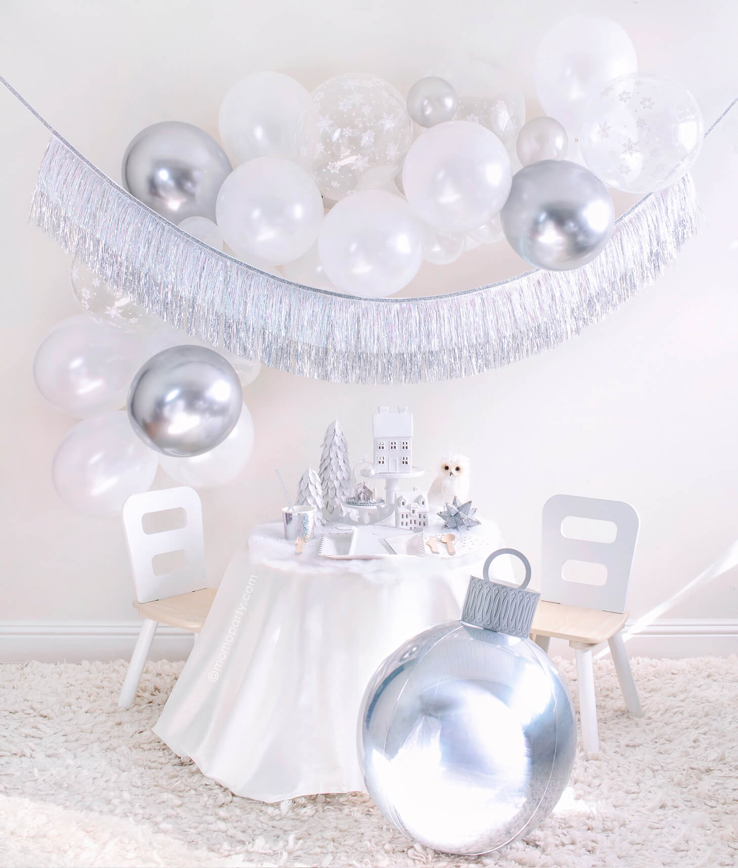 Momopartys 2020 Holiday White Christmas Holiday Box, Small party set up with White Scalloped Large Plates, Silver Sparkle Reindeer Plate, Silver Sparkle Tumbler Cup, Gleaming Large Napkin, Silver Wooden Cutlery and white trees, white house decor on the cake stand, Owl and silver star ornaments on the table, Silver Ornament Foil Balloon in the front. White, silver, snowflake mixed latex balloons cloud, and Silver Tinsel Fringe Garland as wall decoration for a simply modern gorgeous white Xmas party