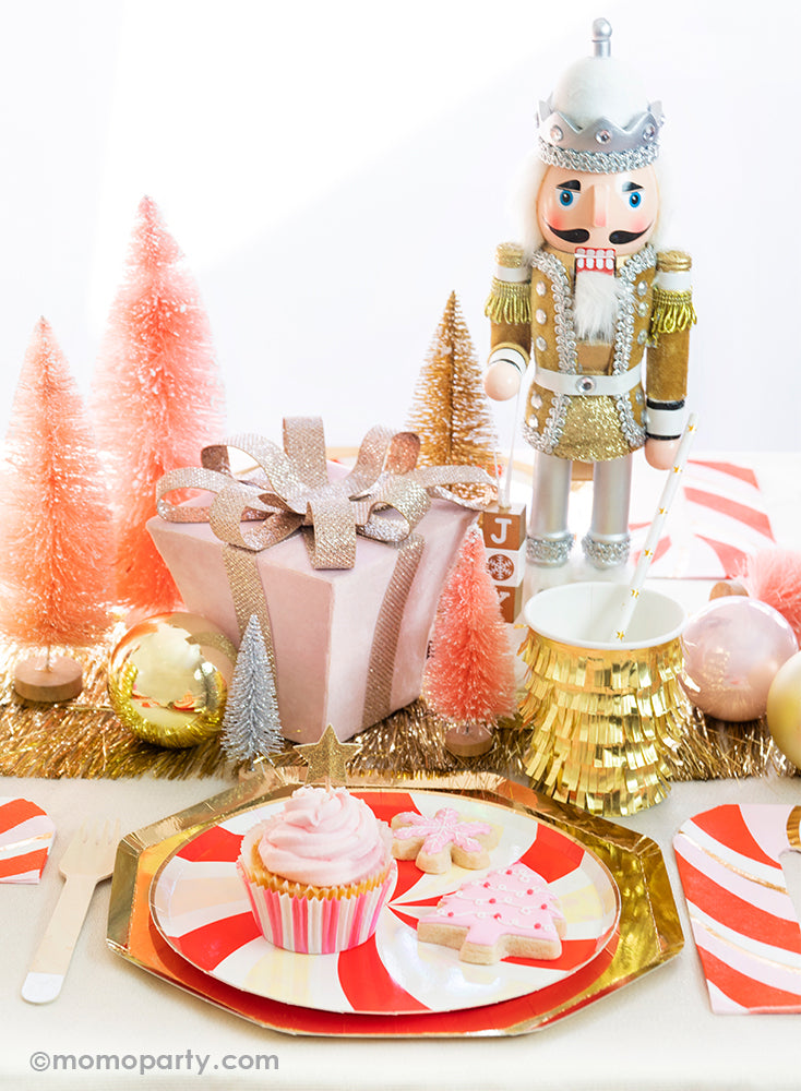 Momopartys Holiday tablescape look with cupcake and pink christmas tree cookie, pink snowflake cookie on the  Peppermint Swirl Side Plates layered on top of Gold Large Dinner Plates, gold fringe cups and peppermint napkin on the side. with a pink christmas gift box, pink and gold Sisal Trees and a Nutcracker as centerpiece, ready for a modern classic look of Gold Red Peppermint Glam Christmas party Celebration
