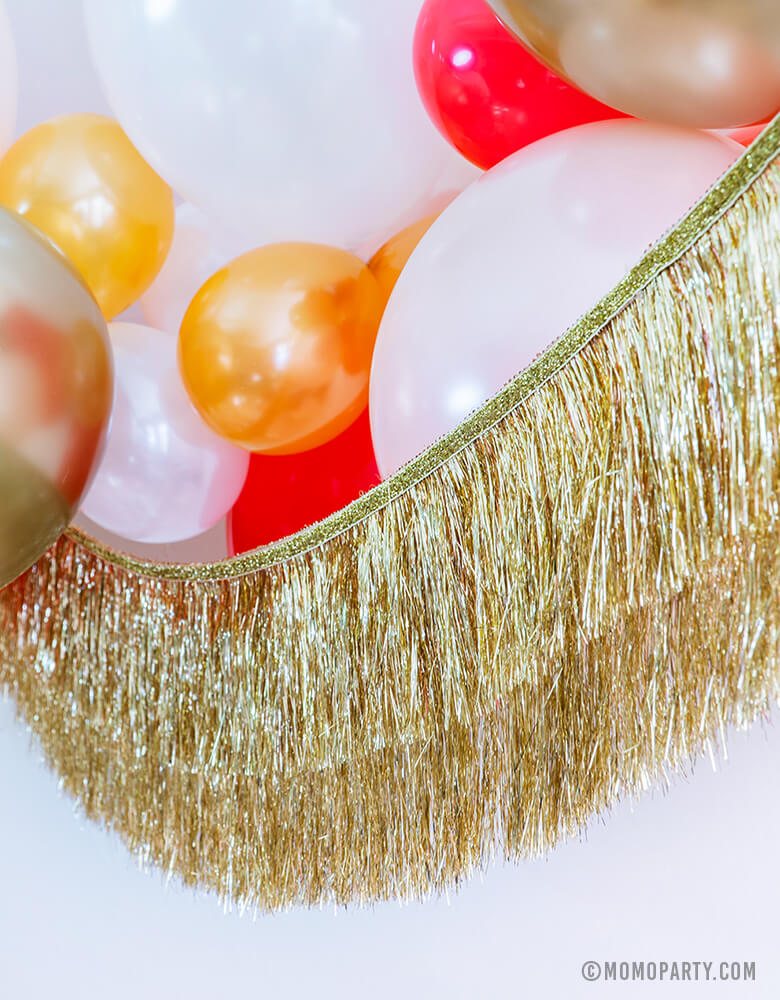Momopartys Holiday party decoration idea feathered Gold, Red, Pearl White, Coral, Pearl peach latex balloons with Meri Meri gold tinsel fringe garland
