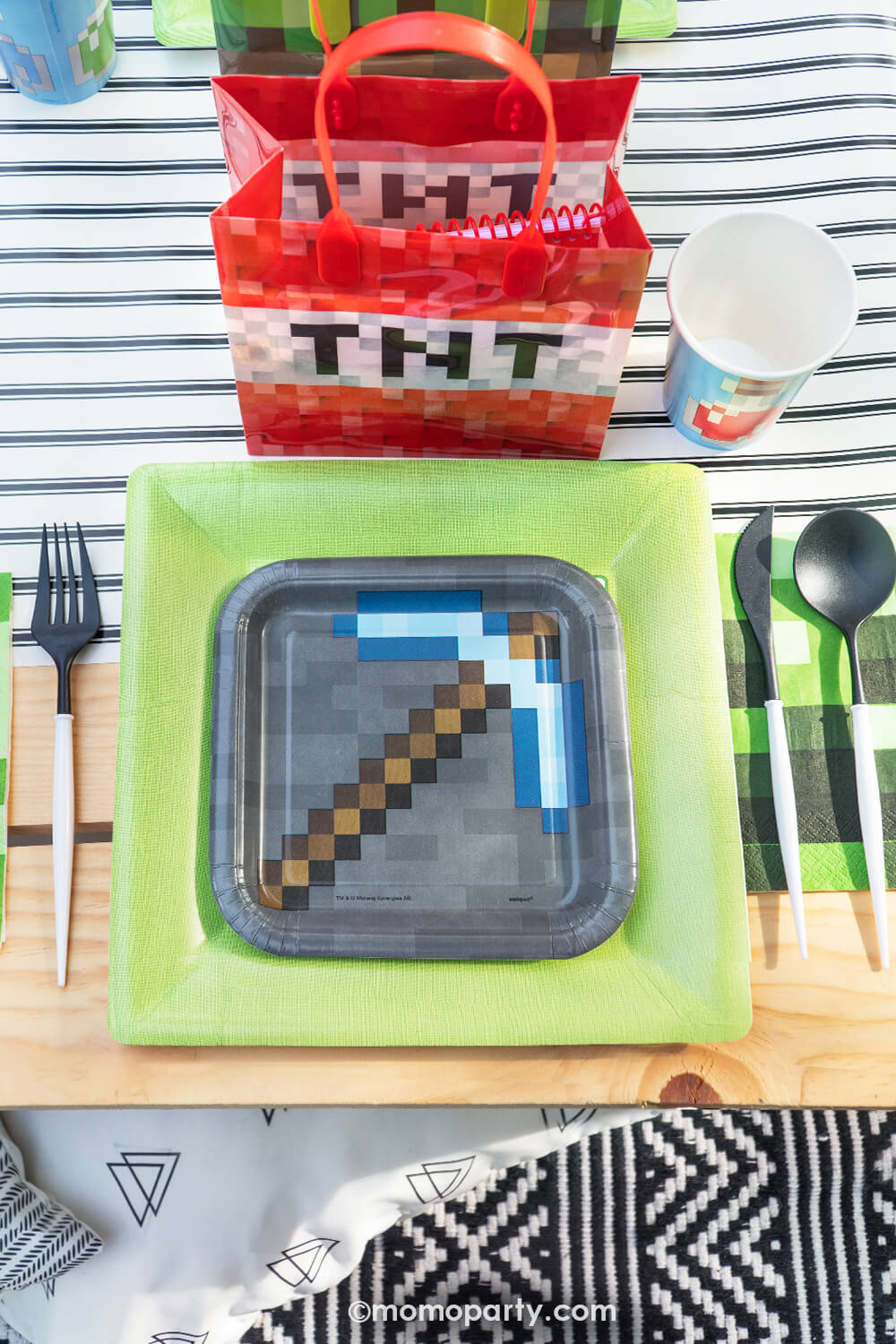 Minecraft themed Birthday Party Ideas by Momopartys. Featuring Minecraft gray side plate layered with modern sophisticated large lime green dinner plates, blue Minecraft potion paper cups, beautiful black and white cutlery sets, an pixel TNT theme goodie bags, all on the black striped table runner of the kids picnic table. These party supplies are perfect for modern kid's minecraft birthday party.