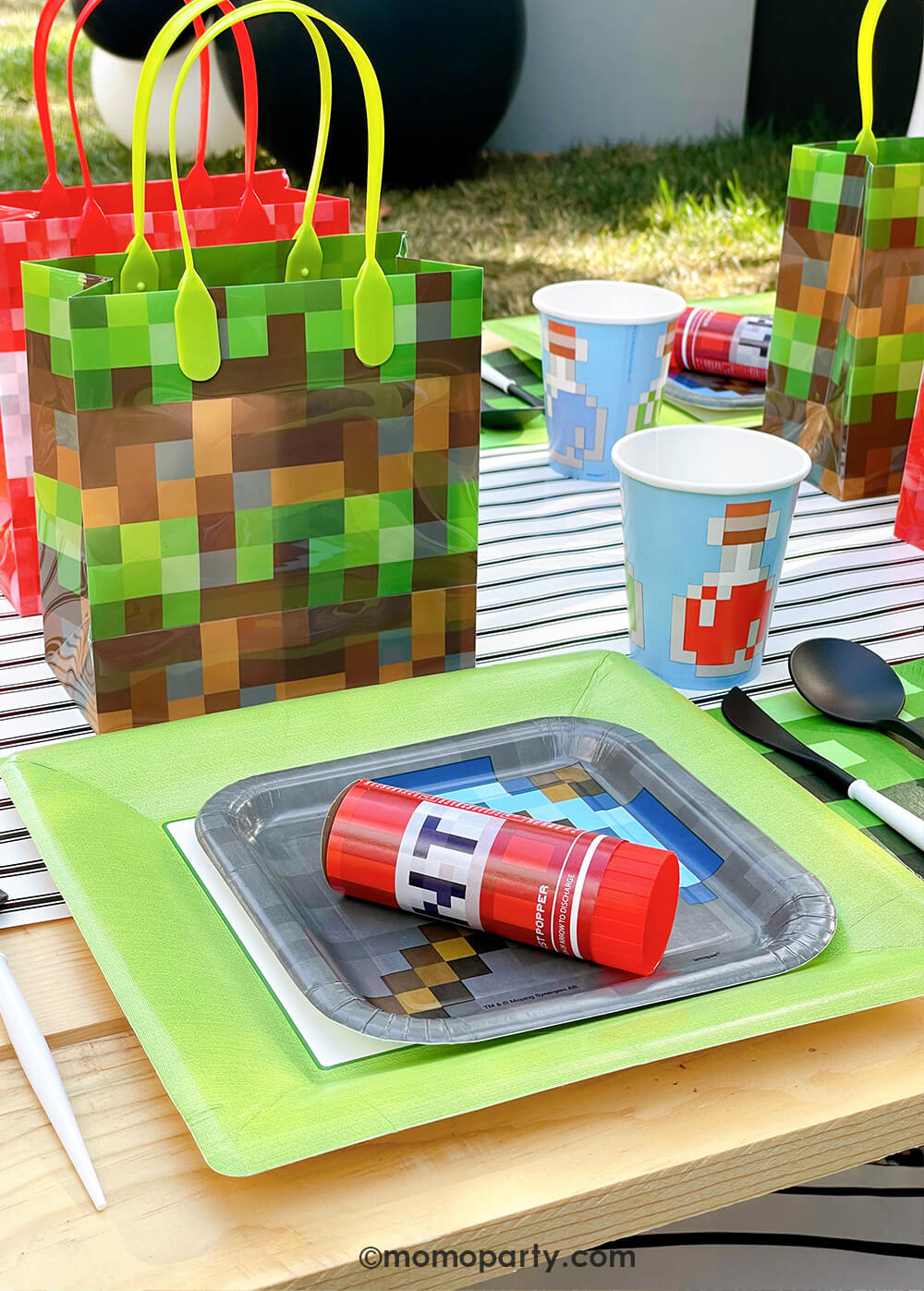 Minecraft themed Birthday Party Ideas by Momopartys. Featuring a fun Minecraft TNT Twist Poppers layered with Minecraft gray side plate and modern sophisticated  large lime green dinner plates, blue Minecraft potion paper cups,  beautiful black and white cutlery sets, an pixel TNT theme goodie bags, all on the black striped table runner of the kids picnic table. 