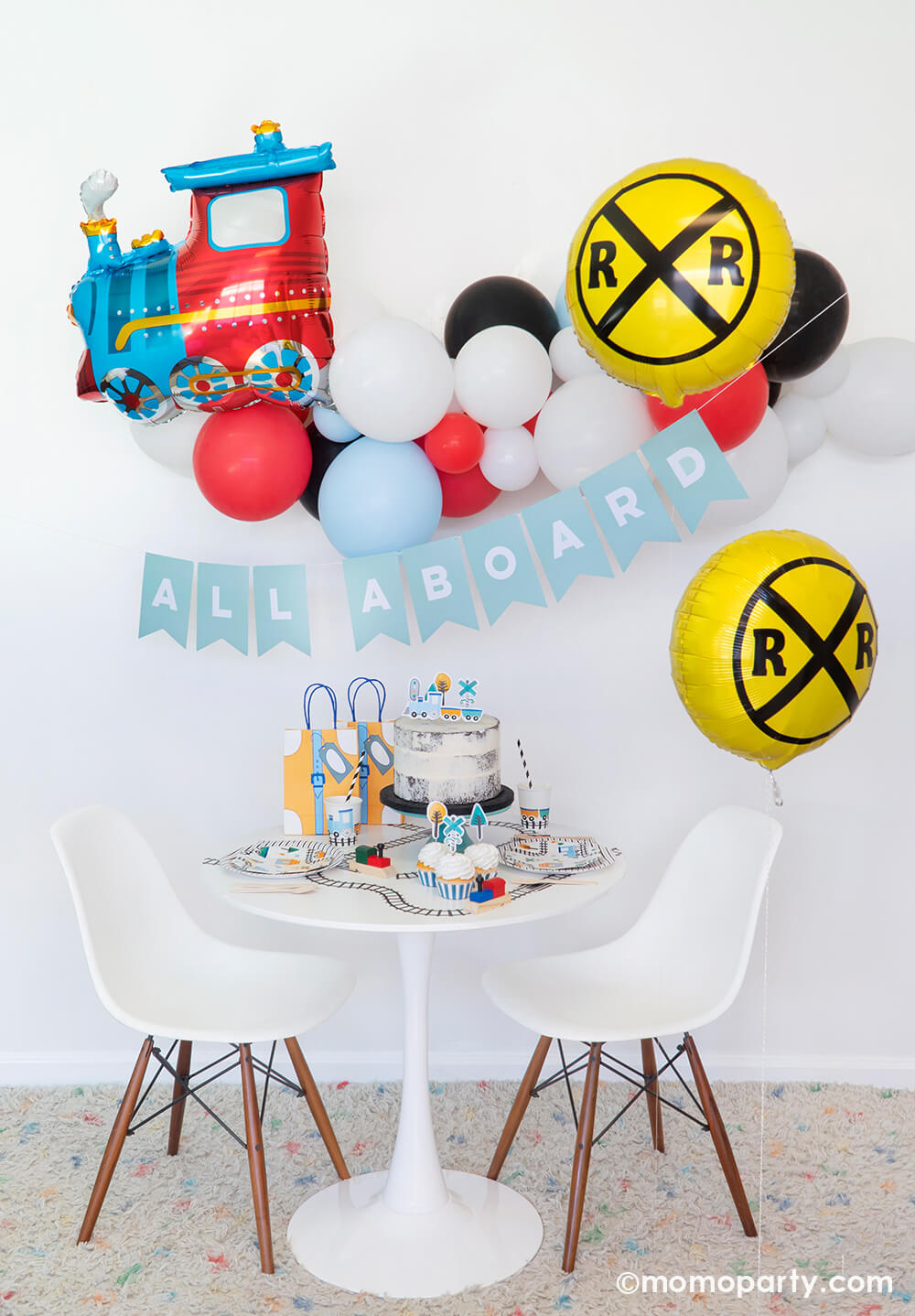 Momopartys Train themed party set up with a choo-choo-train-foil-balloon with classic train balloon garland hanging on the wall, RAILROAD CROSSING SIGN FOIL BALLOONs on the side, a light blue letter board spelled in "all aboard", a white rounded table filled with STEAM TRAIN SMALL PLATES, STEAM TRAIN CUPS, STEAM TRAIN CUPCAKE TOPPERS on the cake and cupcakes, train tape decorated the table top. Such a cute set up for a train themed birthday party, thomas the train birthday party, boy's birthday party