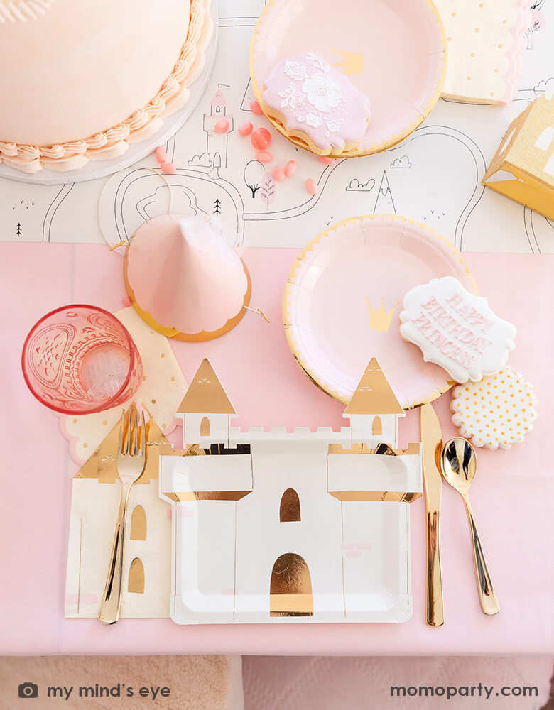 A beautiful tablescape from a girl's princess themed birthday party featuring Momopartys's princess castle shaped large plates, pink princess crown round side plate, turret shaped napkins, a pink princess birthday hat with tulle, in the middle it's a table runner featuring coloring princess fairytale illustrations, all in all makes a great inspiration for kid's princess themed birthday party.