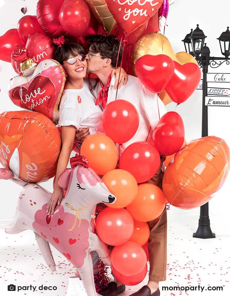 Couple kissing while holding a bouquet of Momopartys's red and pink heart-shaped balloons, celebrating Valentine's Day.
