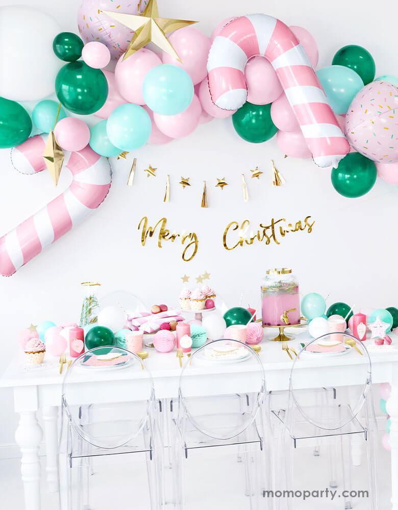 Pink Christmas Party Ideas by Momopartys featuring Party Deco's Pink Candy Cane Foil Balloon on a festive balloon garland in pink, mint and green colors above a festive party table filled with Christmas themed party goods 