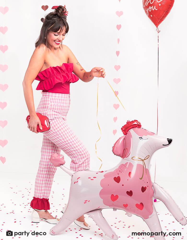 Girl in pink and red outfit happily "walking" Momopartys's 47 x 42.5 inches inches standing pink poodle shaped foil balloon by Party Deco while walking on the street, celebrating Valentine's Day