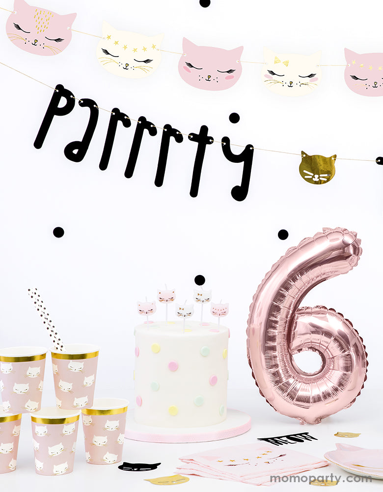 Close up of A kitty cat themed birthday party table. Party Deco Kitty cat garland and Parrrrty time garland decorated on the wall as backdrop, a Rose gold number 6 foil balloon next to a white fondant cake decorated with polka dots and kitty cat candles, party deco cat plates, napkins and cups in the front of the table. These cat themed party supplies are super cute for a girls birthday, cat lover's birthday, pet themed party