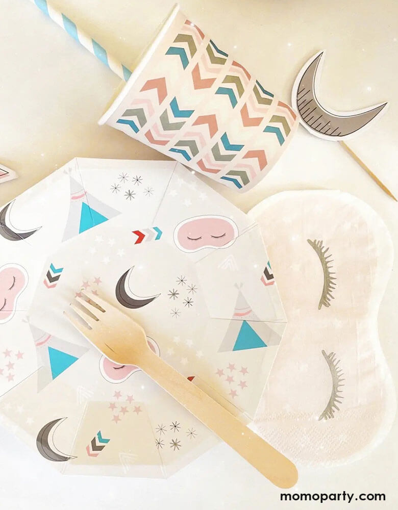 A tablescape of girls sleepover party featuring Momopartys's sleepover napkins in the shape of sleeping masks by Pooka Party, along with coordinated plates featuring  sleepover themed illustrations like sleeping tents, sleeping masks, moons and stars, plus light pink party cups with chevron design, and cupcake topers with moon design, perfect for girl's slumber party.