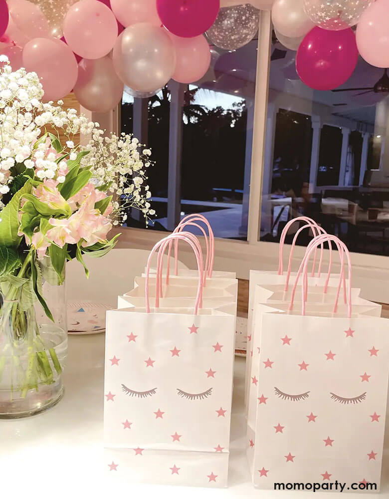 A sleepover slumber party featuring Momopartys's 8.2 x 5.9 x 3.15 inches sleepover party bags with sleepy eyes and pink star designs by Pooka Party, comes in set of 8. In the background the room was decorated with pink, rose, and rose gold balloon garland with beautiful flower bouquet, makes a great inspiration for girls birthday party ideas.