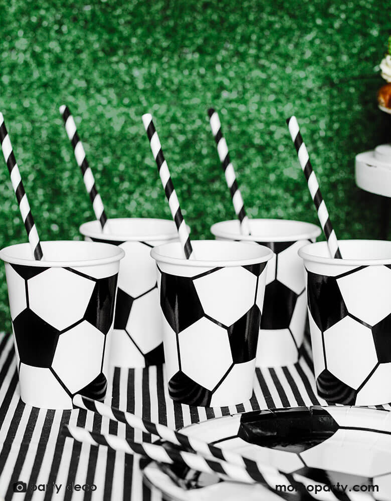 A table filled with soccer themed tableware including  Momopartys's 6.8 oz Soccer ball party cups by Party Deco in classic black and white color, perfect for a kid's soccer themed birthday party or a World Cup soccer watching party!