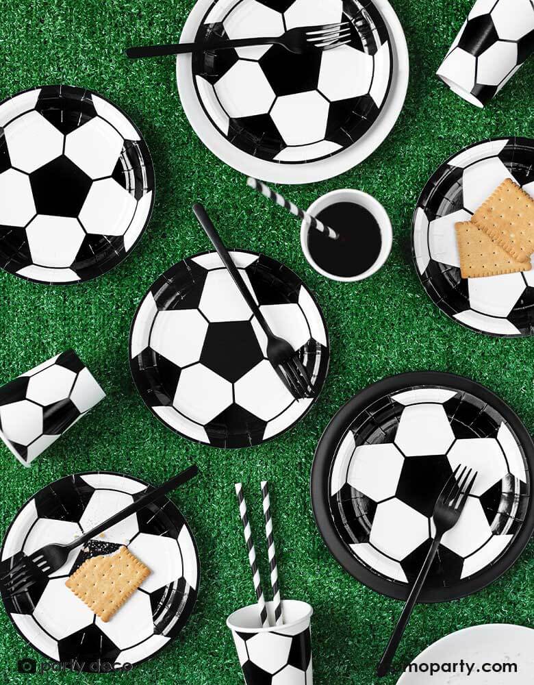 A table with filled with soccer themed tableware including  Momopartys's 6.8 oz Soccer ball party cups by Party Deco in classic black and white color, perfect for a kid's soccer themed birthday party or a World Cup soccer watching party!