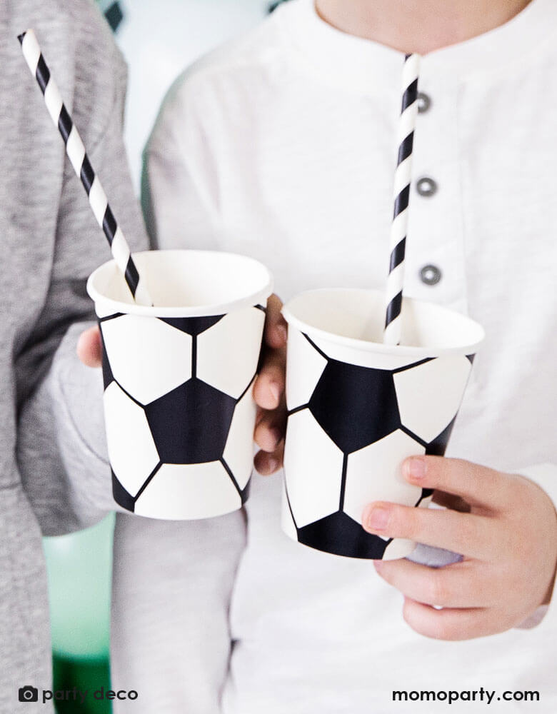 Two boys holding  Momopartys's 6.8 oz Soccer ball party cups by Party Deco in classic black and white color, perfect for a kid's soccer themed birthday party or a World Cup soccer watching party!