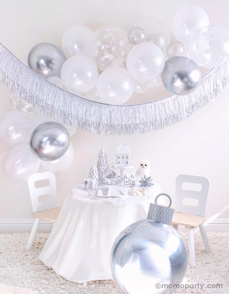 Momopartys 2020 Holiday White Christmas Holiday Box, Small party set up with White Scalloped Large Plates, Silver Sparkle Reindeer Plate, Silver Sparkle Tumbler Cup, Gleaming Large Napkin, Silver Wooden Cutlery and white trees, white house decor on the cake stand, Owl and silver star ornaments on the table, Silver Ornament Foil Balloon in the front. White, silver, snowflake mixed latex balloons cloud, and Silver Tinsel Fringe Garland as wall decoration for a simply modern gorgeous white Xmas party